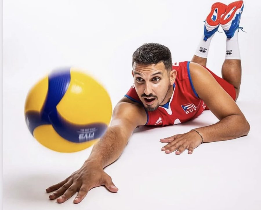 Dennis Del Valle dives with an outstretched arm to reach a volleyball during a match.